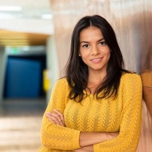 Portrait of a happy casual businesswoman standing with arms folded in hallway and looking at camera